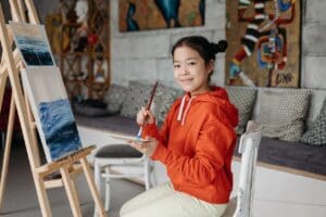Female child painting on a canvas wearing orange jumper